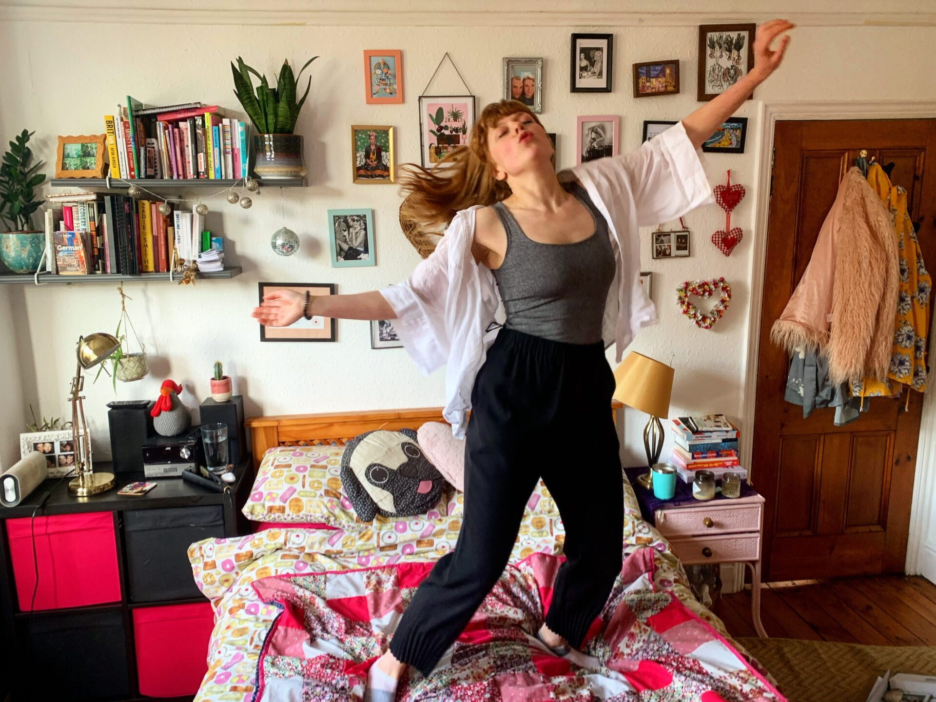 Woman dancing on a bed in a cozy looking bedroom, she looks blissful with long flowing hair