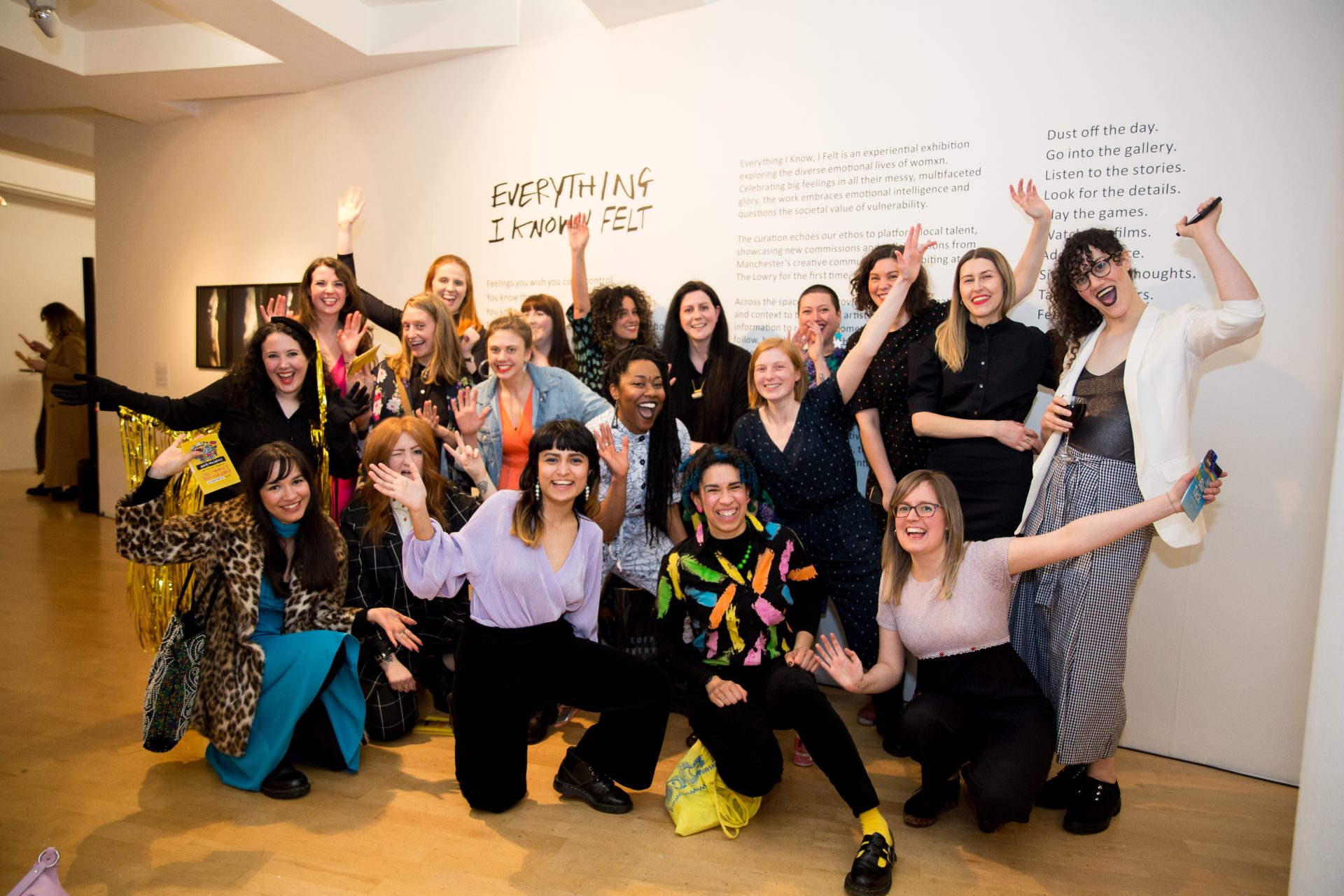 19 people grouped together for a team photo in an art exhibition, all smiling some with arms in the air