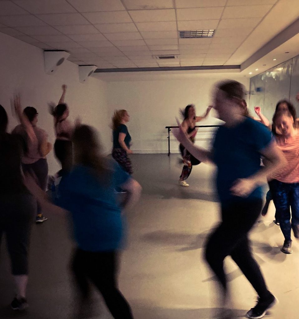 Group of people moving quickly in a circle with arms in the air wearing sports wear, they are blurred