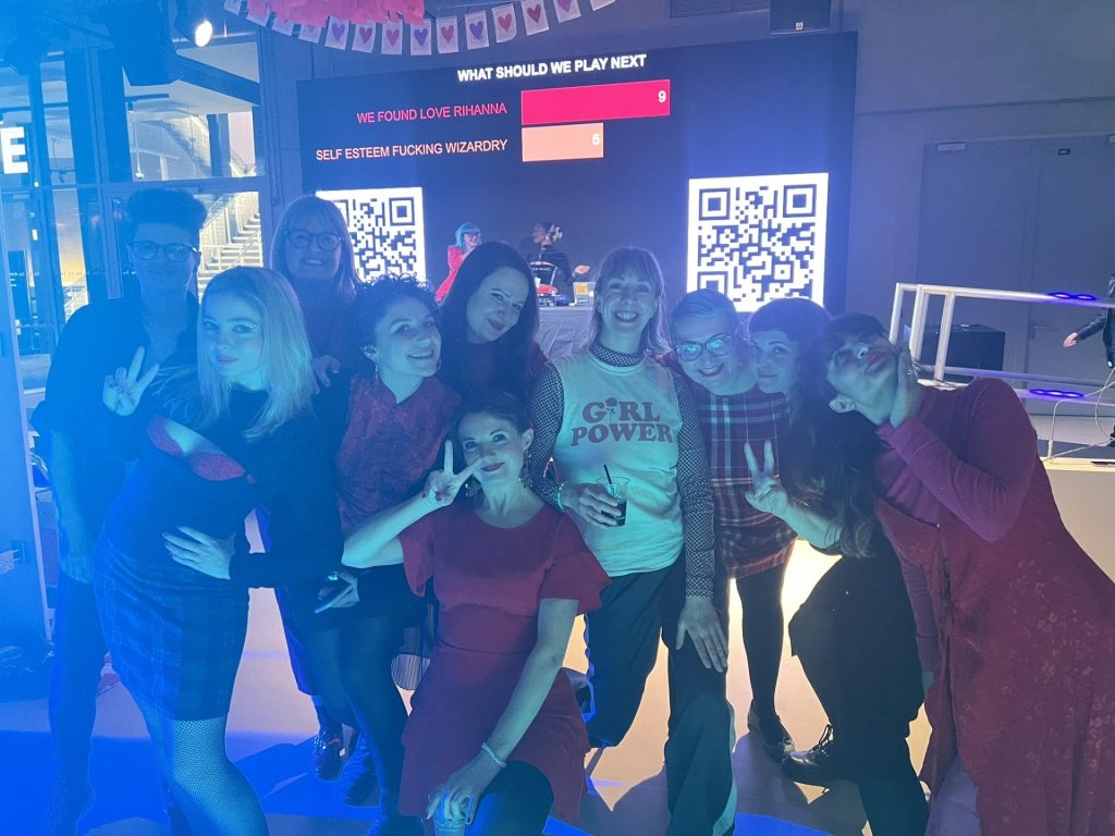 10 people posing for group photo, smiling and all wearing red clothes under blue light